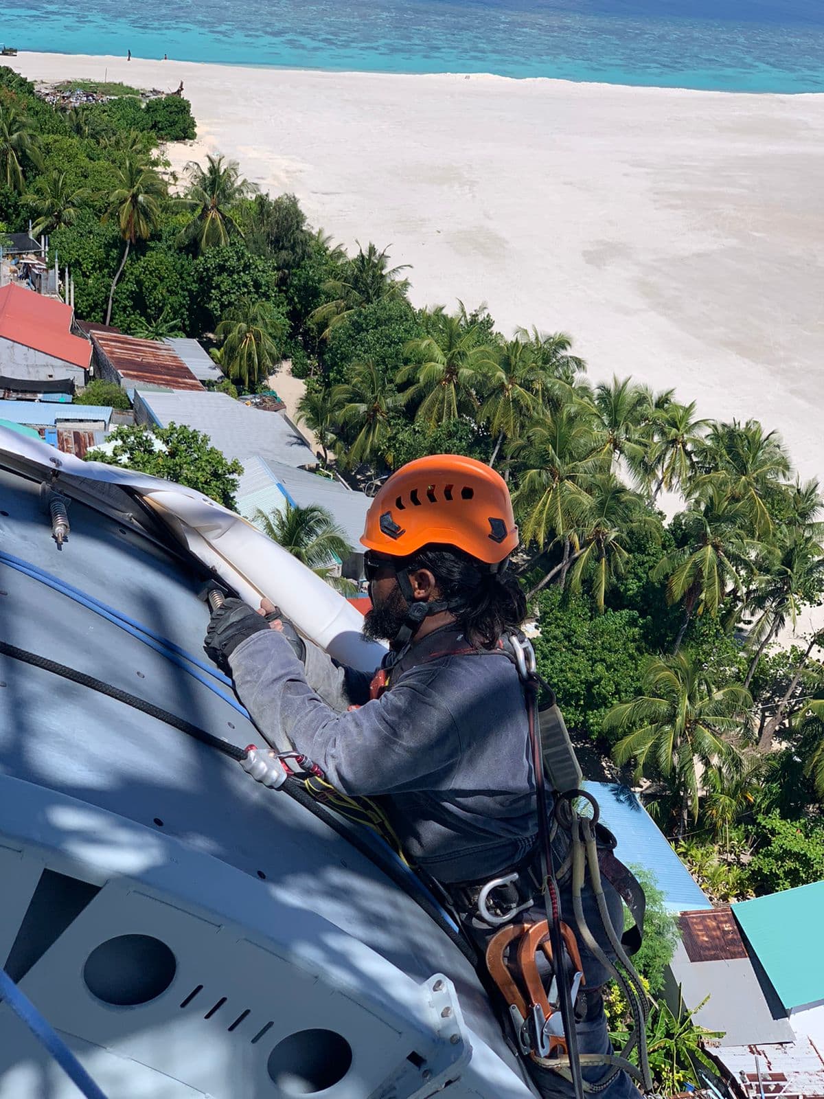 Rishthaa technician on rope access working at the head of a telecom tower above a Maldivian island